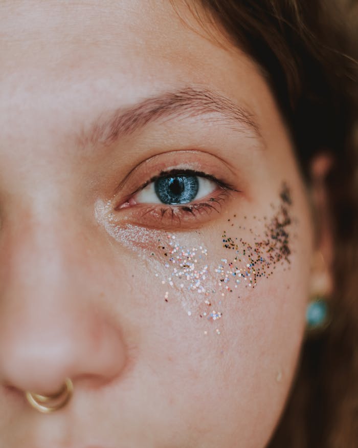 Closeup of crop anonymous young female with piercing and shiny glitters on face  looking at camera in daylight