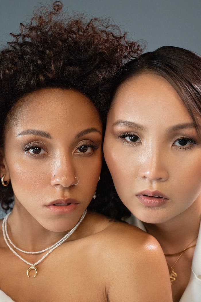 Close-up portrait of two women with jewelry and natural makeup, highlighting diversity and style.